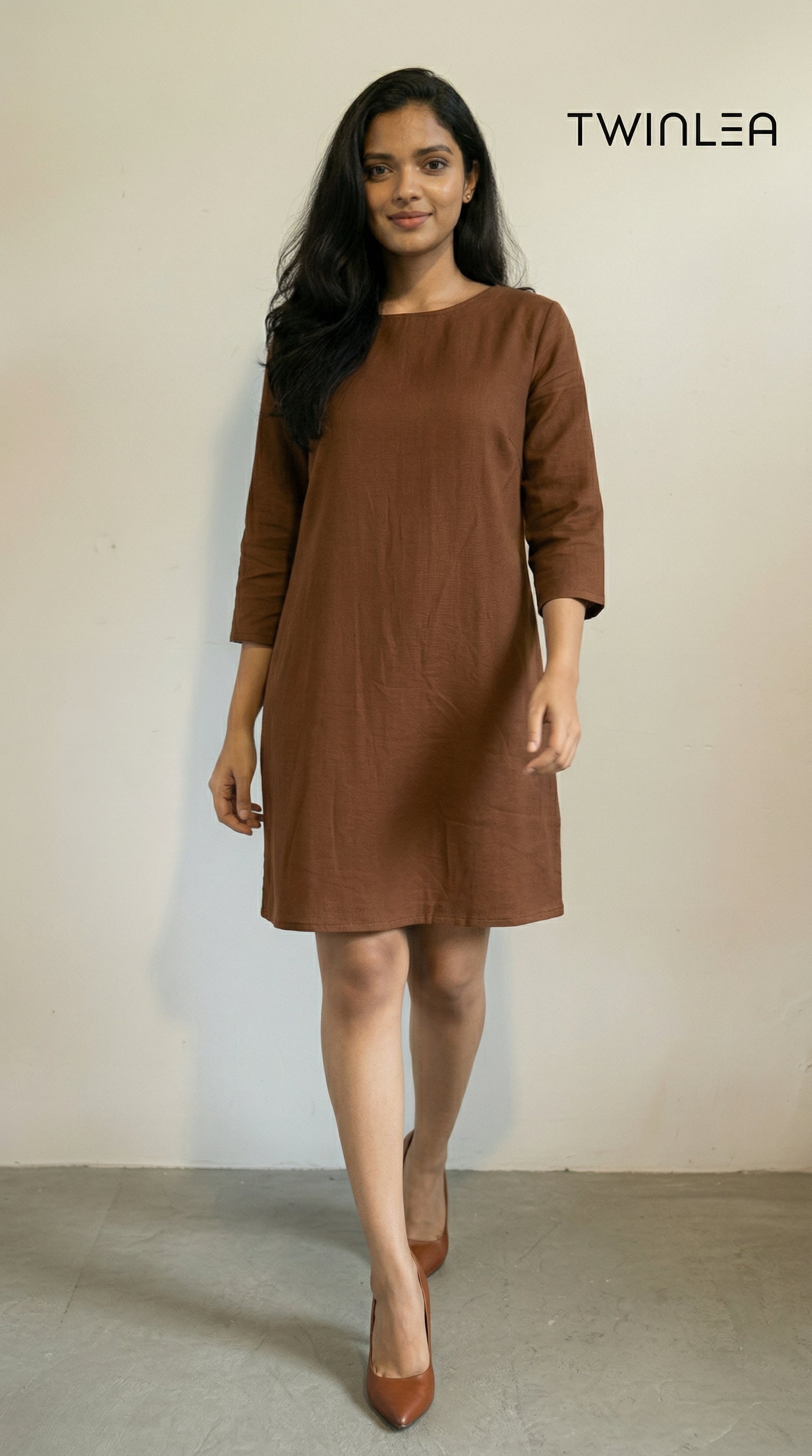 Model wearing a brown dress with a plain background, featuring the brand 'TWINLEA'.