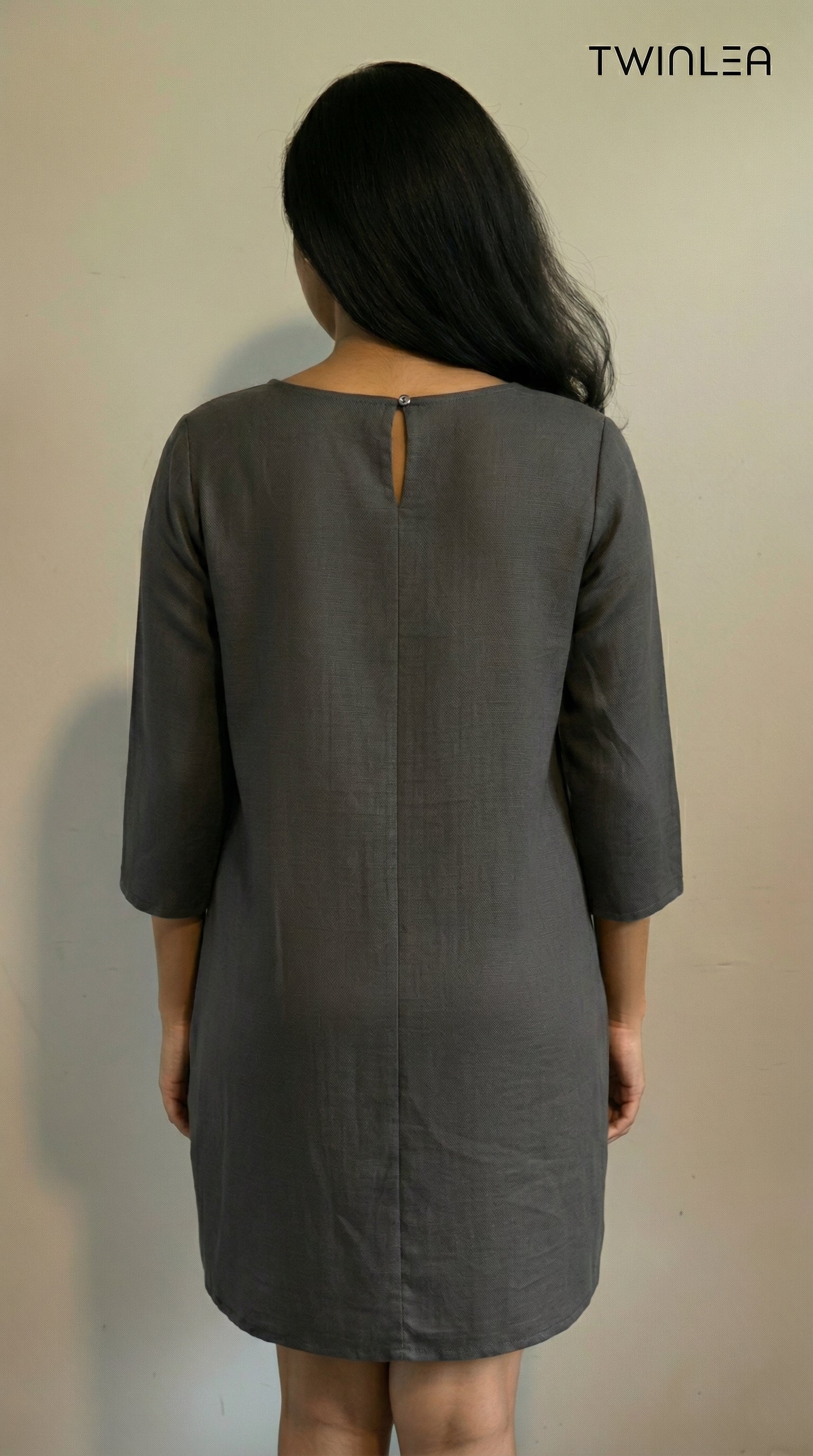 Model wearing a gray dress with a cut-out back detail, standing against a plain background.
